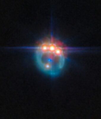L’Anello Prezioso Creato da un Quasar Una piccola immagine di una galassia distorta dalla lente gravitazionale in un anello fioco. Nella parte superiore dell'anello ci sono tre punti molto luminosi con punte di diffrazione che fuoriescono da essi, uno accanto all'altro: in realtà si tratta di copie di un singolo quasar nella galassia, duplicate dalla lente gravitazionale. Al centro dell'anello, la galassia ellittica che esegue la lente appare come un piccolo punto blu.